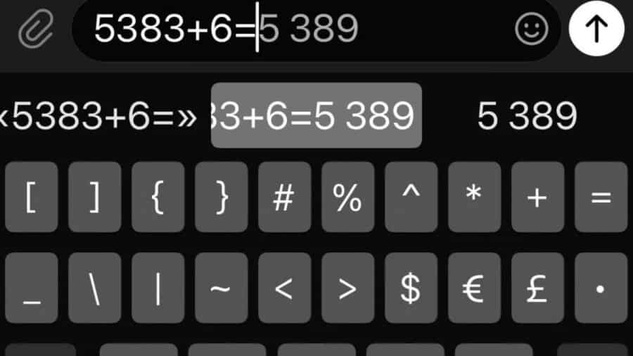 Tastiera di iPhone in modalità scura mentre viene digitata un’operazione matematica; nei suggerimenti compare il risultato “5 389” direttamente sopra i tasti.