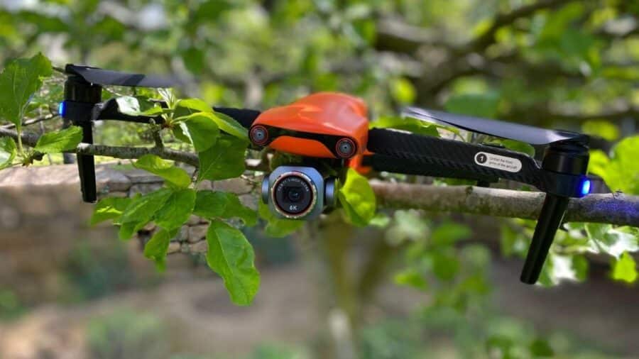 Drone Autel Evo Lite+ arancione con fotocamera 6K sospeso tra rami e foglie in un ambiente naturale.