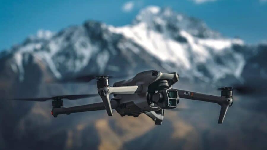 DJI Air 3S in volo davanti a montagne innevate, con doppia fotocamera frontale e bracci aperti.