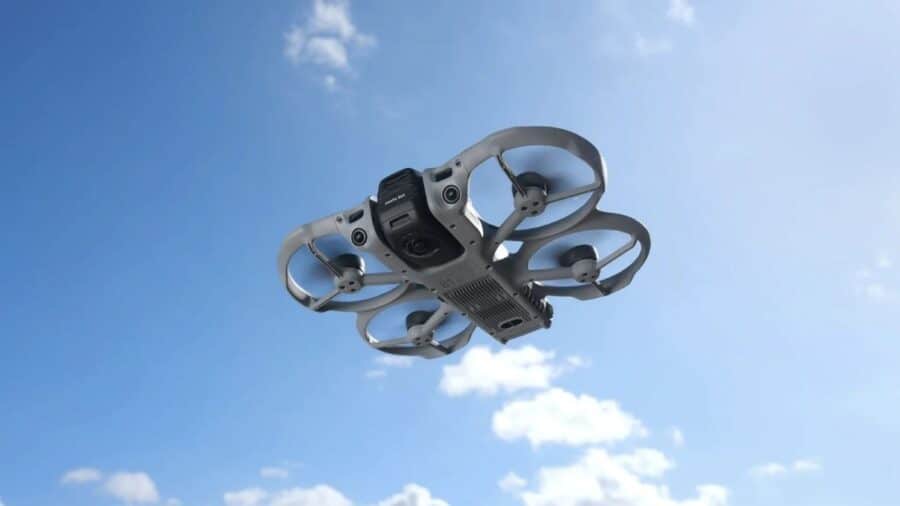 DJI Avata 360 visto dal basso mentre vola nel cielo azzurro, con paraeliche integrati e struttura compatta.