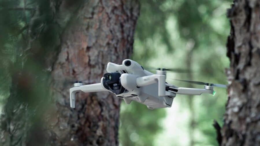 DJI Mini 4 Pro in volo tra gli alberi, con fotocamera stabilizzata e luci di posizione verdi.