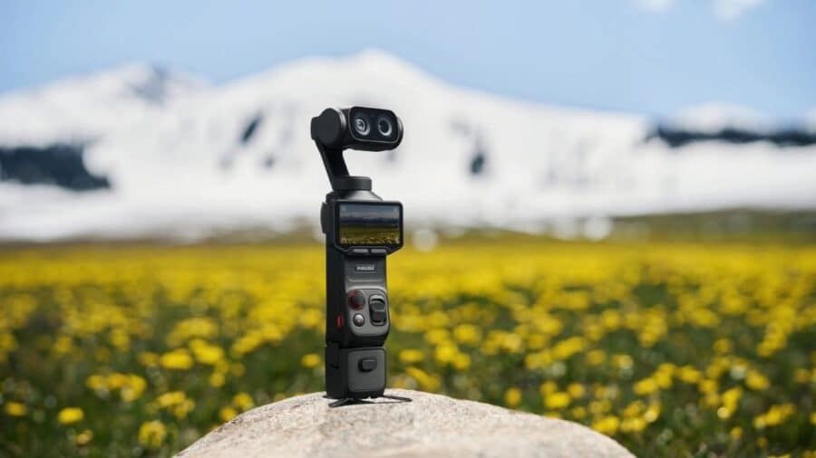 Insta360 Luna Ultra posizionata su una roccia in un prato fiorito, con montagne innevate sfocate sullo sfondo.