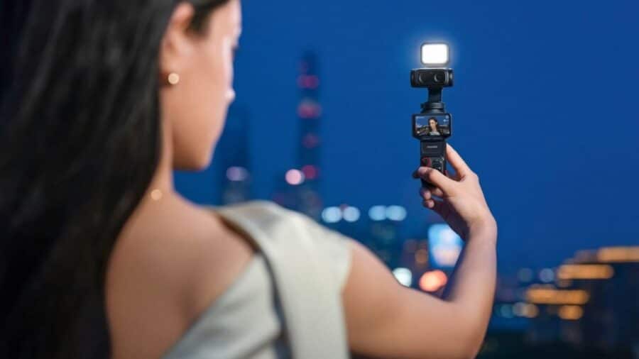 Una donna registra un video notturno con Insta360 Luna Ultra dotata di luce LED, con skyline urbano sfocato sullo sfondo.