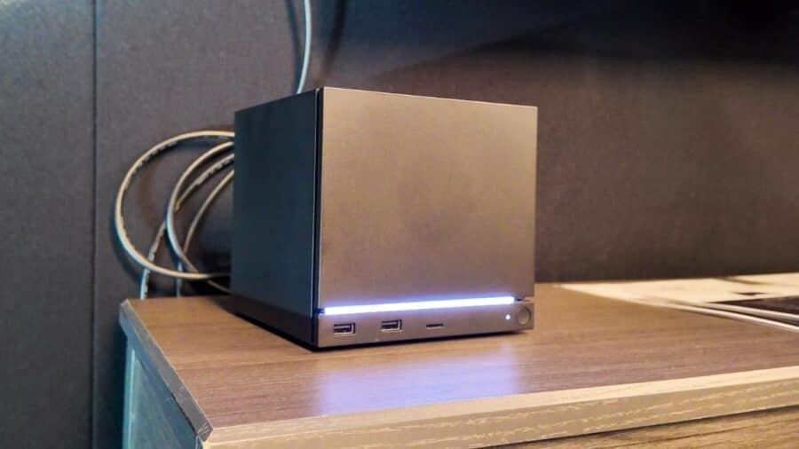 Steam Machine nera appoggiata su un mobile TV, con barra LED frontale accesa e porte USB visibili nella parte anteriore.