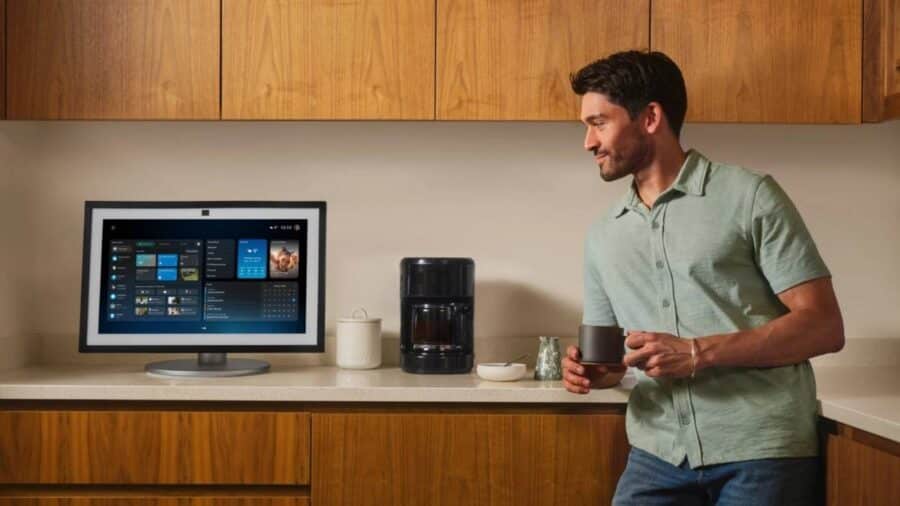 Uomo in cucina usa Alexa+ su uno smart display mentre beve una tazza, con interfaccia dell’assistente visibile sullo schermo.