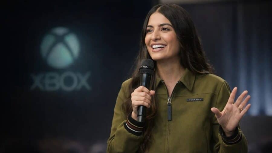 Dirigente Xbox con microfono durante una presentazione pubblica, con il logo Xbox sfocato sullo sfondo.