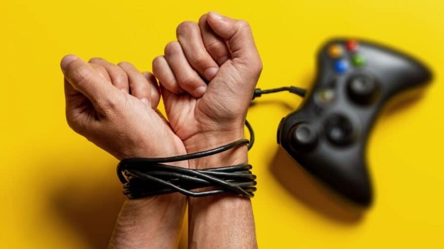 Mani legate dal cavo di un controller da gaming su sfondo giallo.