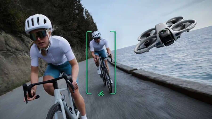DJI Avata 360 in volo accanto a due ciclisti su una strada costiera, con tracciamento del soggetto evidenziato sullo schermo.