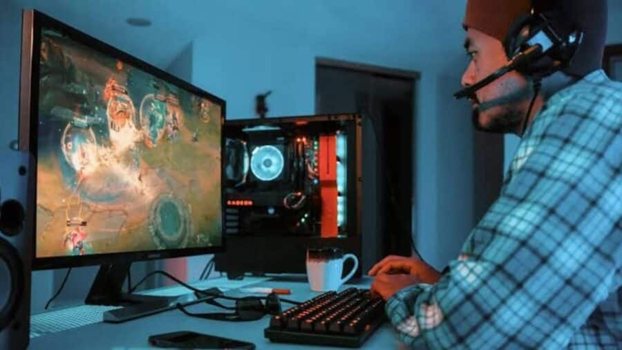 Giocatore PC con cuffie e tastiera meccanica davanti a un monitor gaming, durante una sessione di gioco in una stanza illuminata da luci blu e rosse.