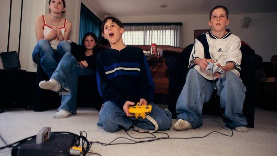 Ragazzi degli anni ’90 giocano insieme davanti alla televisione con controller cablati, durante una sessione multiplayer in salotto.