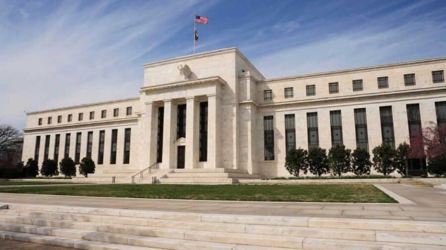 Facciata monumentale in marmo bianco della sede centrale della Federal Reserve a Washington, caratterizzata da grandi finestre, rigide colonne e la bandiera degli Stati Uniti che sventola sul tetto.