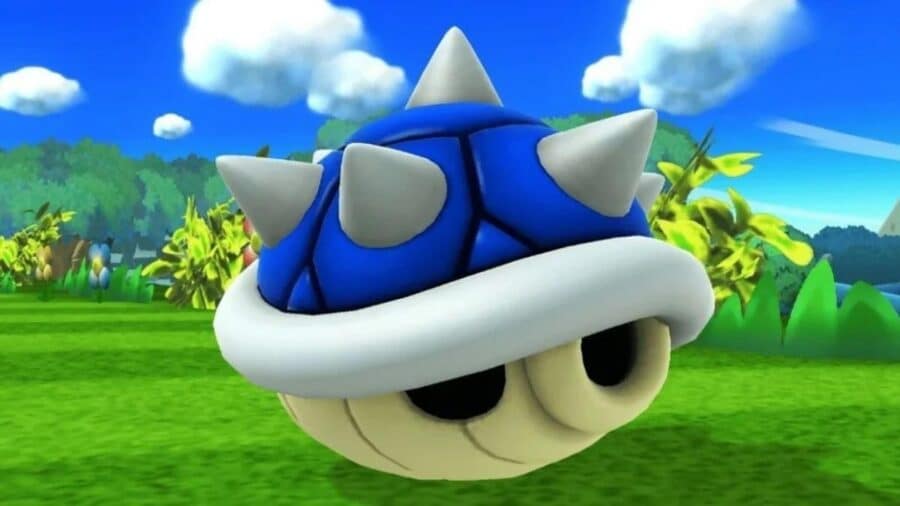 Primo piano del Guscio Blu di Mario Kart, con corazza blu e spuntoni bianchi, sospeso sopra un prato verde.