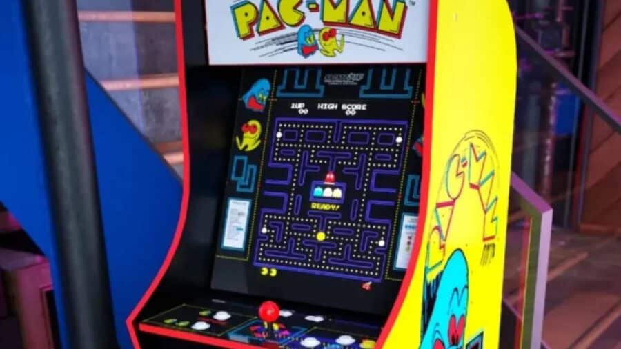 Dettaglio di un cabinato arcade di Pac-Man di colore giallo acceso, decorato con le storiche grafiche originali sui lati e con lo schermo acceso sulla schermata iniziale della partita.