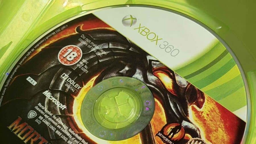 Primo piano di un disco fisico del videogioco Mortal Kombat per Xbox 360, riposto all'interno della sua classica custodia in plastica verde fluo.