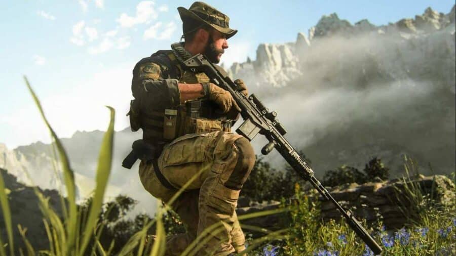 Un soldato in tenuta tattica militare e cappello a tesa larga, tratto dal videogioco Call of Duty, è inginocchiato nell'erba alta e impugna un fucile di precisione sullo sfondo di imponenti montagne rocciose.