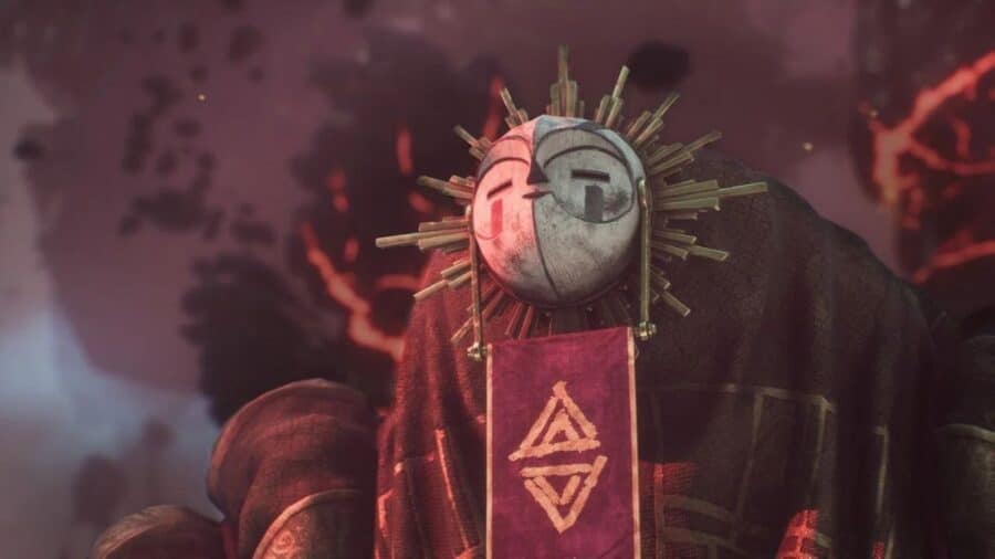 Dettaglio artistico di un misterioso personaggio videoludico che indossa una suggestiva maschera circolare a forma di sole stilizzato, avvolto in un mantello scuro da cui pende uno stendardo rosso con un simbolo geometrico.