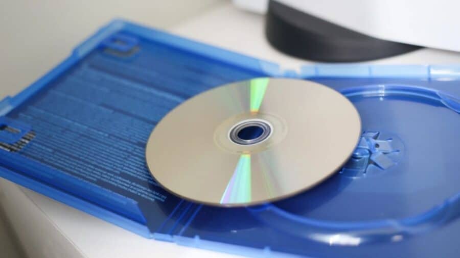 Disco ottico di un videogioco PlayStation appoggiato al contrario con il lato riflettente verso l'alto, sopra la sua tipica custodia in plastica blu aperta.
