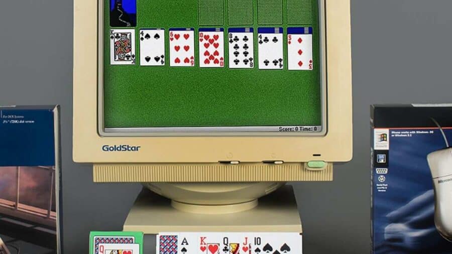 Postazione informatica vintage con un vecchio monitor CRT GoldStar che visualizza una partita al Solitario di Windows, affiancato dalla scatola originale di un Microsoft Mouse degli anni '90 e carte da gioco reali.