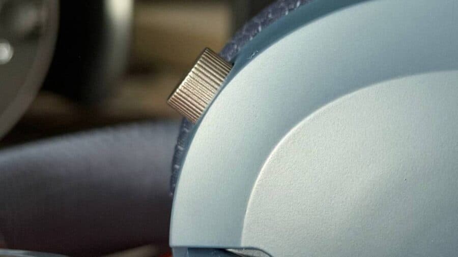 Primo piano del piccolo pulsante multifunzione metallico e zigrinato, sporgente dal profilo curvo del padiglione auricolare sinistro delle cuffie MSI Maestro 500.
