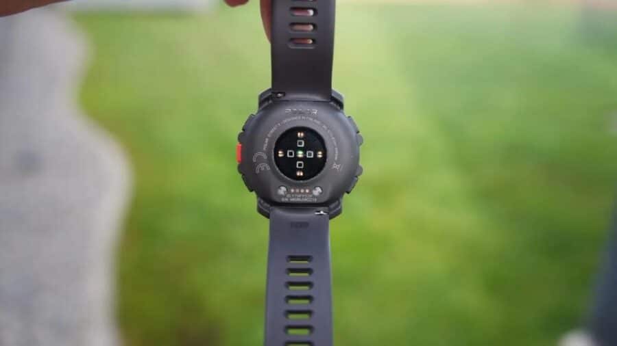 L'orologio Polar Street X tenuto tra le dita in verticale per mostrare il retro della cassa, dove si illumina il sensore ottico per la misurazione della frequenza cardiaca con i suoi LED verdi e rossi.