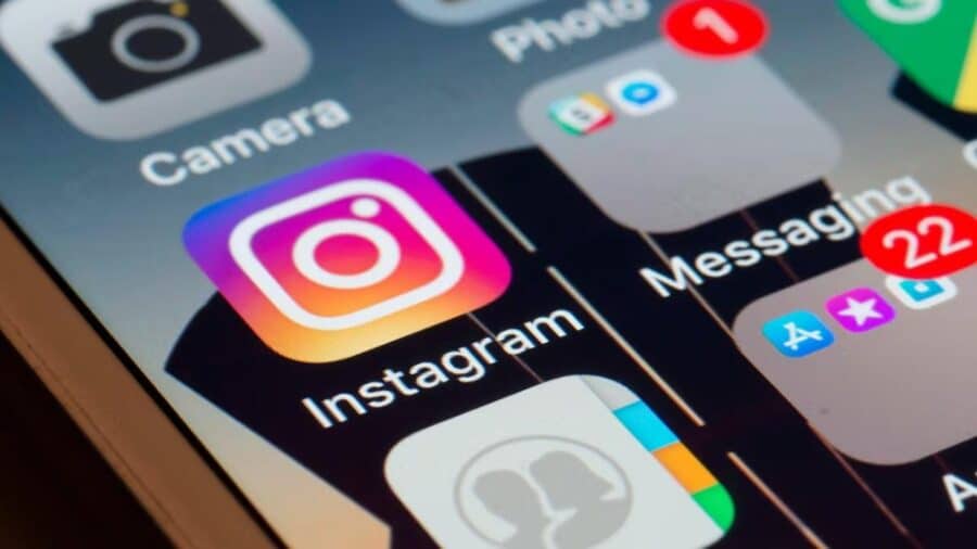 Primo piano dello schermo di uno smartphone che mostra la celebre icona colorata dell'app di Instagram, circondata da altre applicazioni come Fotocamera e Messaggi.