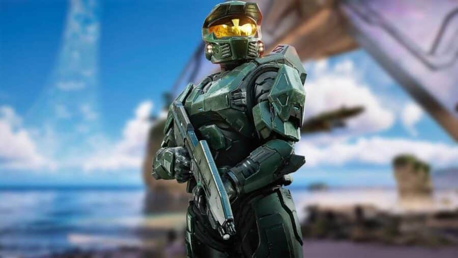 Master Chief in armatura verde scuro impugna un fucile d'assalto in posa eroica su una spiaggia, con le nuvole e la gigantesca struttura dell'anello visibili in lontananza.