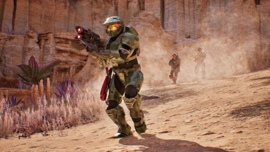 Master Chief corre in un canyon desertico polveroso impugnando un'arma Covenant aliena rossa, seguito da due Marine alleati durante un'intensa scena di battaglia in pieno giorno.