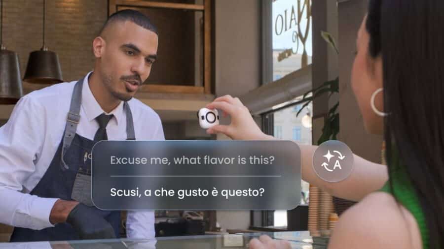 Una ragazza tiene in mano la piccola videocamera bianca Insta360 GO Ultra, rivolgendola verso il commesso di una caffetteria. In sovraimpressione compare un pop-up grafico che mostra la traduzione simultanea di una domanda dall'inglese all'italiano.