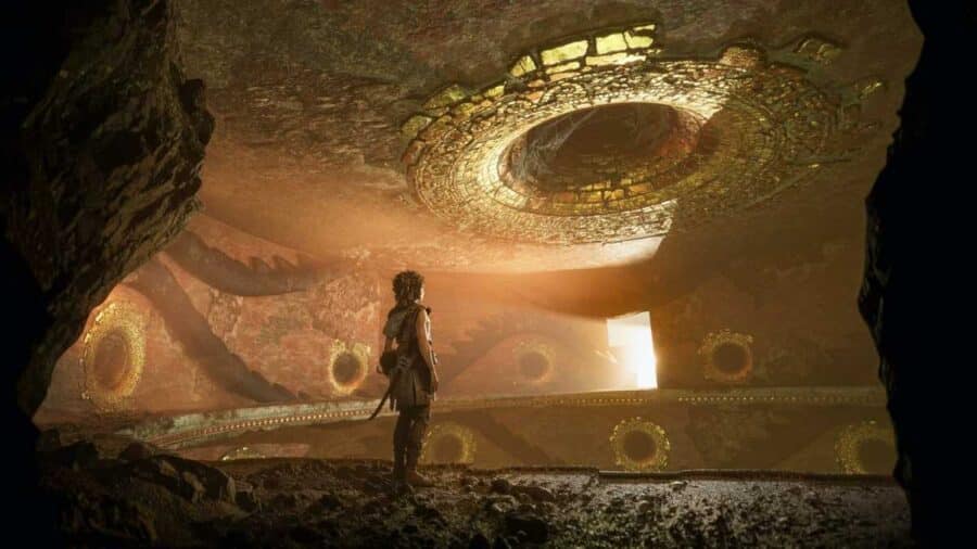 Sophia osserva l'interno di un'antica struttura sotterranea illuminata da un grande oculo dorato circolare sul soffitto da cui filtra un raggio di luce naturale.