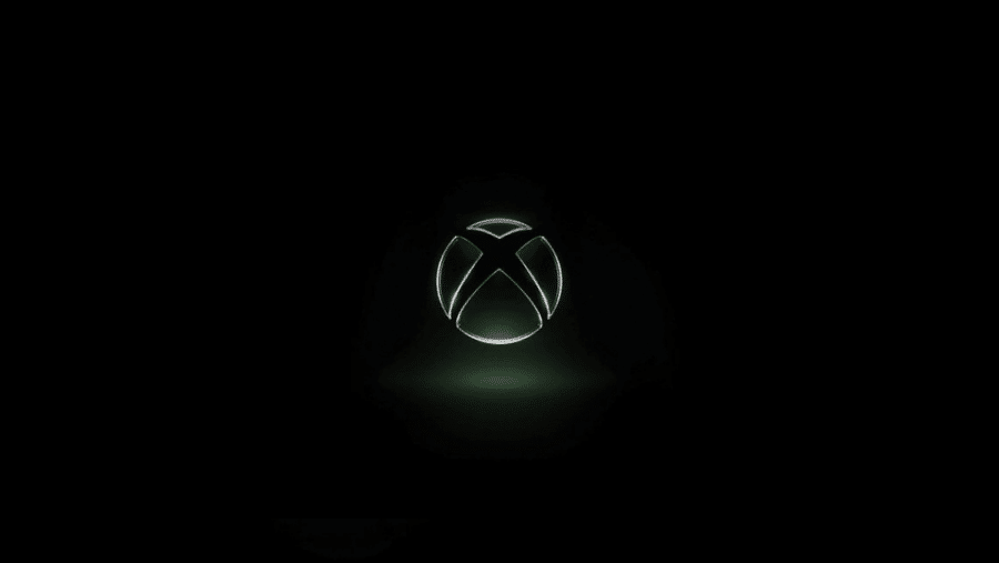 Logo sferico di Xbox con incisione a X metallica illuminata al centro, posizionato su uno sfondo scuro con un leggero bagliore verde inferiore.