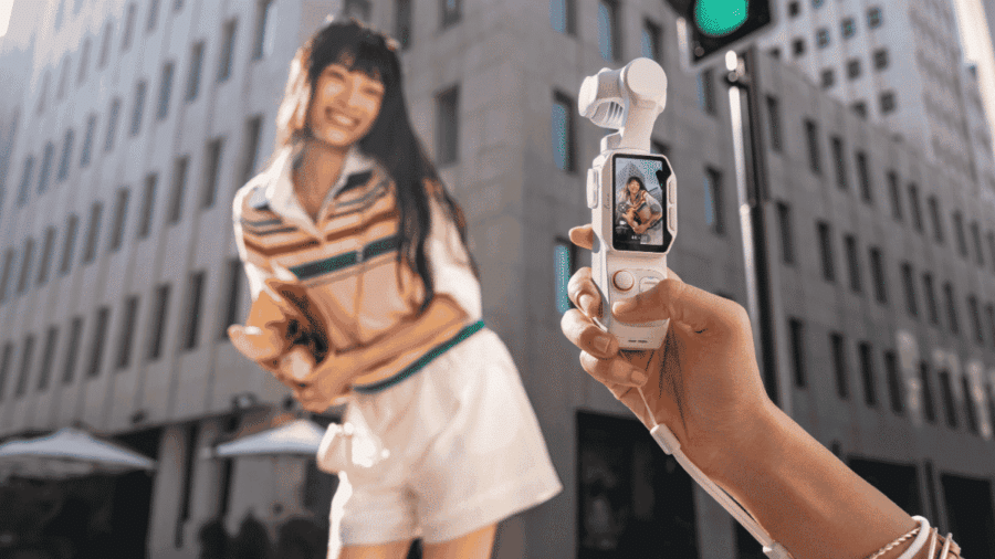 Ripresa ravvicinata di una mano che regge la Insta360 Luna Pro per inquadrare in verticale una ragazza sorridente che cammina per strada tra gli edifici del centro urbano.