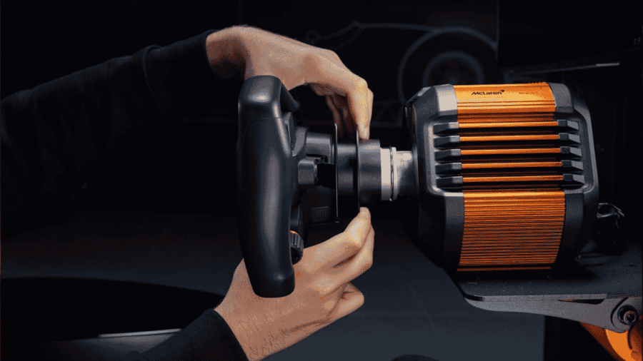Un piano ravvicinato delle mani di un utente che collegano un volante da corsa modular-style a una base Direct Drive di colore arancione McLaren Racing e grigio scuro, mostrando il meccanismo di aggancio.