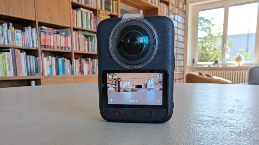 DJI Osmo 360 II appoggiata su un tavolo con lo schermo posteriore acceso, obiettivo anteriore in primo piano e libreria sullo sfondo.