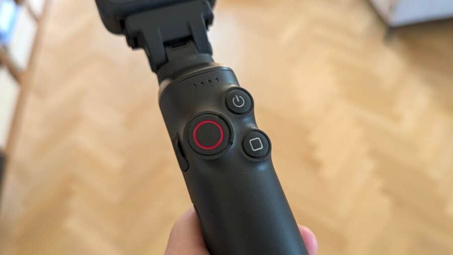 Primo piano dell'impugnatura del bastone selfie con pulsante di accensione, pulsante di registrazione con anello rosso e pulsante di stop, indicatori LED della batteria.