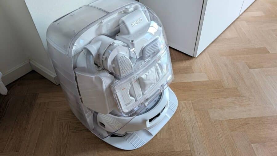Base station di Romo P2 vista dall'alto con pannelli trasparenti che mostrano il meccanismo interno, il robot ROMO agganciato e i flaconi di soluzione detergente e deodorante pavimenti.