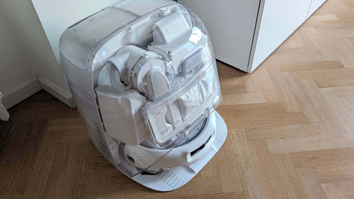 Base station di Romo P2 vista dall'alto con pannelli trasparenti che mostrano il meccanismo interno, il robot ROMO agganciato e i flaconi di soluzione detergente e deodorante pavimenti.