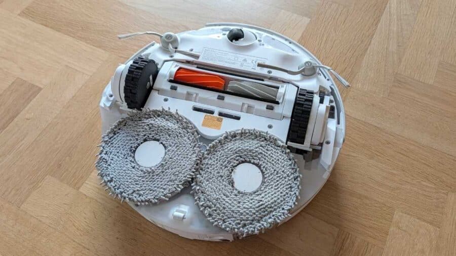 Vista dal basso del robot con i due panni lavapavimenti, la spazzola centrale a listelli con anti-groviglio arancione e la spazzola laterale.