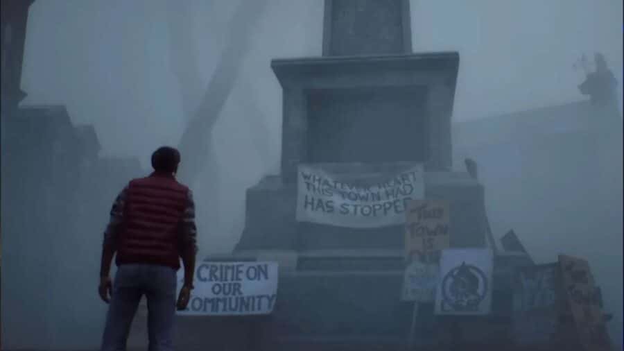 Simon visto di spalle mentre osserva un monumento in pietra avvolto dalla foschia, su cui sono affissi cartelli di protesta contro i crimini aziendali verso la comunità.
