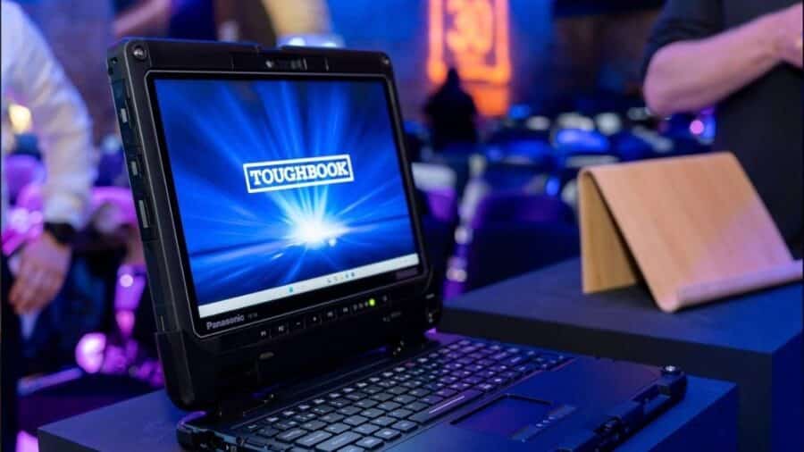 Primo piano del 2-in-1 Panasonic Toughbook 34 agganciato alla tastiera opzionale su un piedistallo dell'evento, con schermo da 12,4 pollici acceso sul logo Toughbook.