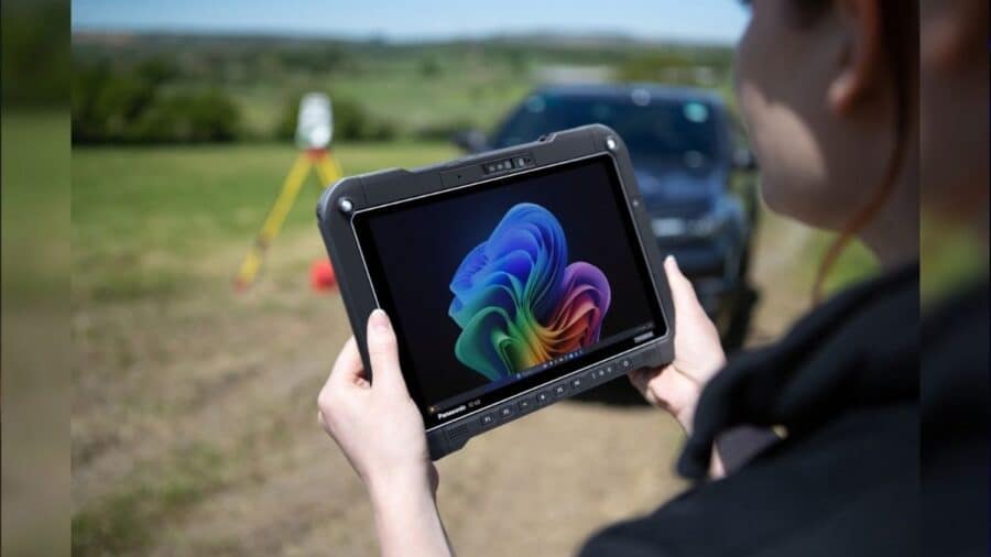 Un operatore sul campo tiene tra le mani il tablet Toughbook G3 all'aperto, con un veicolo fuoristrada e una stazione topografica su treppiede visibili sullo sfondo sfocato